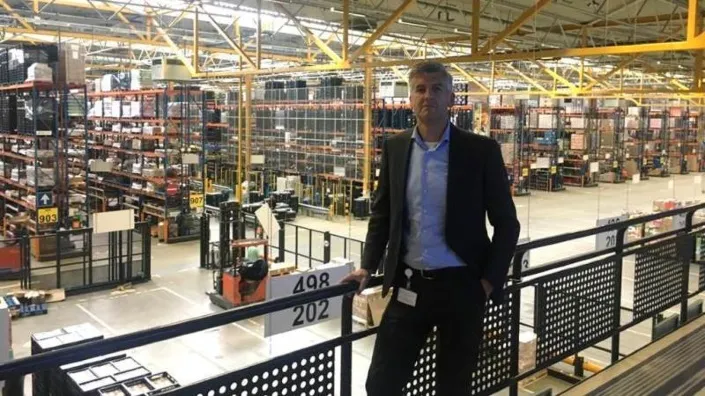 Michiel Kooijman, implementatiemanager bij Gom, kijkt uit over een groot distributiecentrum met stellingen en heftrucks.