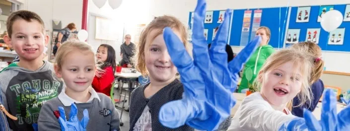 blije kinderen in een schoolklas met schoonmaakhandschoenen aan