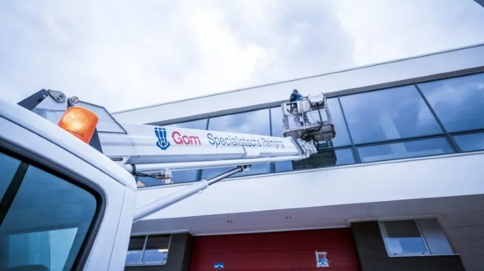 Medewerker van Gom Specialistische Reiniging reinigt ramen van een hoog gebouw met behulp van een hoogwerker