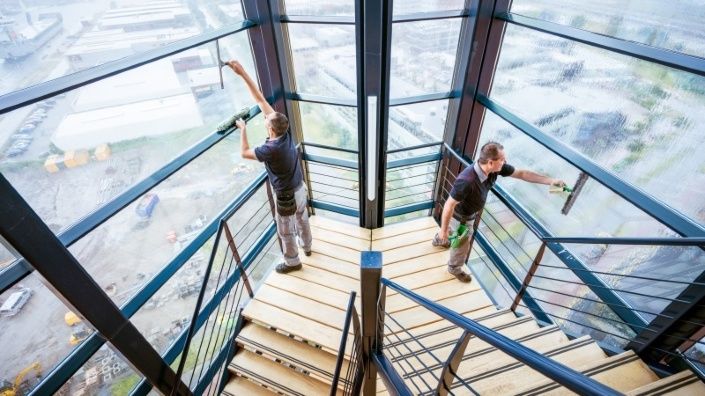 Twee medewerkers van Gom glas en gevelreiniging zijn ramen aan het zemen in het trappenhuis