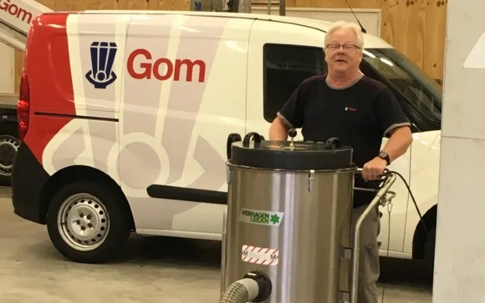Henk Pronk, allround handyman bij Gom Specialistische Reiniging, aan het werk in een werkplaats met een industriële reinigingsmachine voor een bedrijfswagen met Gom-logo.