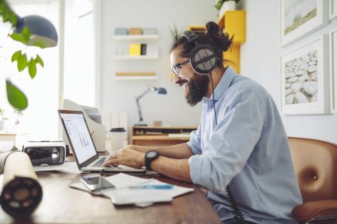 Een man met baard en koptelefoon op zijn oren aan het werk achter een laptop