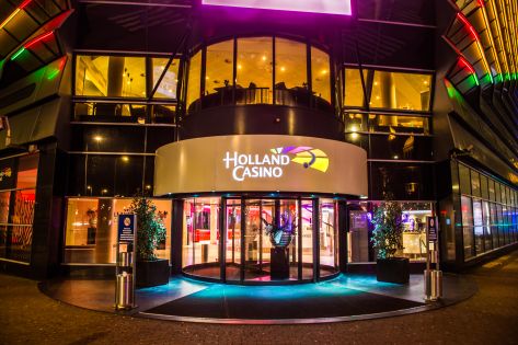 De voorkant van een Holland Casino waarbij je kijkt op de draaideur met daarboven het logo.