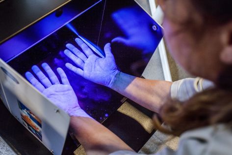 een mevrouw controleert aan de hand van uv-stralen of zij haar handen goed gewassen heeft