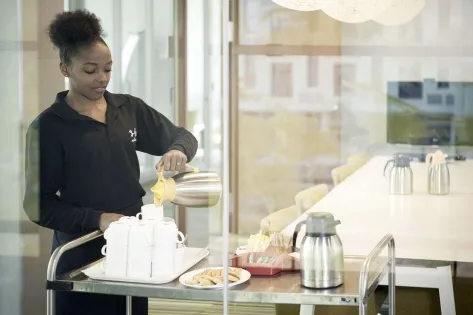 een studente schenkt koffie vanuit een koffiekan in