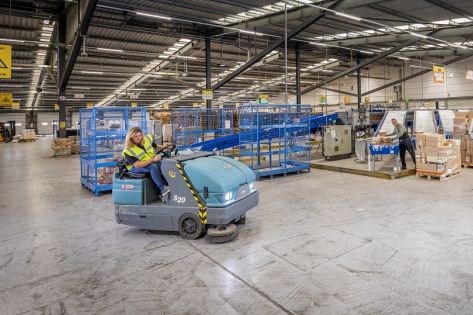 een medewerker van Gom Logistiek zit op een schrobzuigmachine en schrobt de vloer in de bedrijfshal