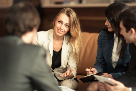 Een viertal collega's die in een informele zetting (bank en lage tafel) met elkaar in overleg zijn.