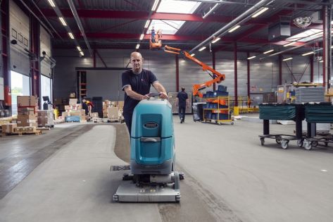 een medewerker van Gom Logistiek loopt achter een schrobzuigmachine en maakt hiermee de vloer van een distributiecentrum schoon