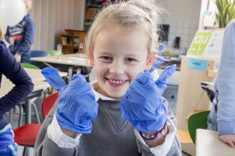 Een leerling van een basisschool met schoonmaakhandschoenen aan steekt beide duimen omhoog