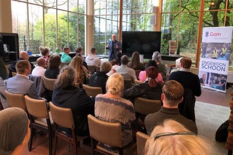 een groep rayonleiders met de rug naar je toe, zit te luisteren naar een man