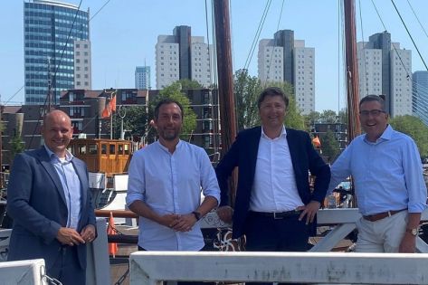 Vier mannen kijken lachend in de camera met de skyline van Rotterdam achter zich