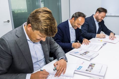 3 personen zitten aan tafel en tekenen een contract