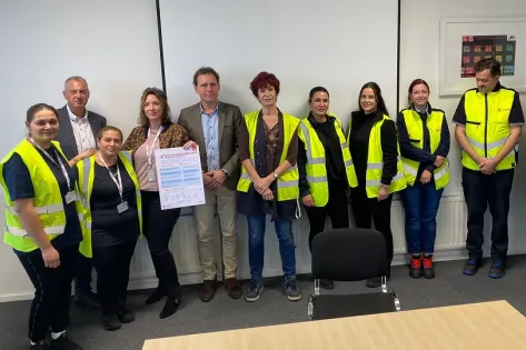 Een groep schoonmaakmedewerkers en managementteamleden staan met de ondertekende veiligheidsbelofte in hun handen