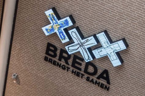 Een muur met 3 witte kruizen met tekeningen boven de woorden 'Breda brengt het samen'