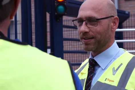 Mannelijke beveiliger staat uniform met een geel hesje te praten met een collega beveiliger.