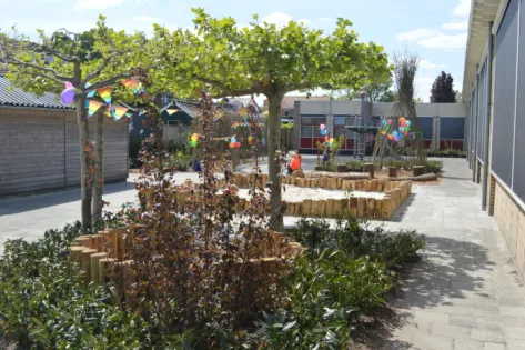 Schoolplein van basisschool De Hoeksteen in Heerenveen, opnieuw ingericht met bomen, speelplekken en kleurrijke versiering om natuurlijk spelen te stimuleren.