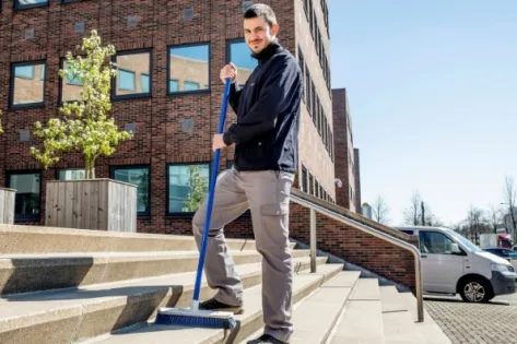 Medewerker van Gom Openbare Ruimten veegt de trappen bij een kantoorpand, symbool voor de uitbreiding met huismeesterdiensten.