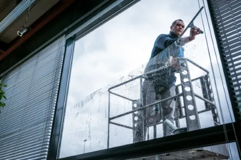 Glazenwasser maakt grote ramen schoon terwijl hij op een hoogwerker staat buiten een gebouw.