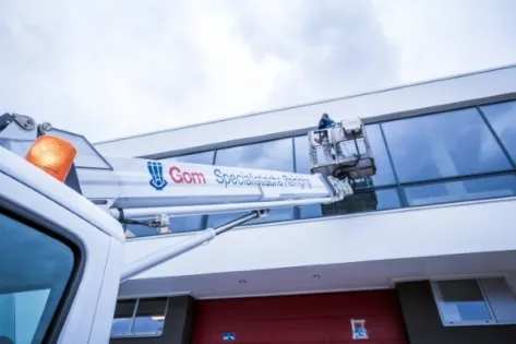 Medewerker van Gom Specialistische Reiniging reinigt ramen van een hoog gebouw met behulp van een hoogwerker