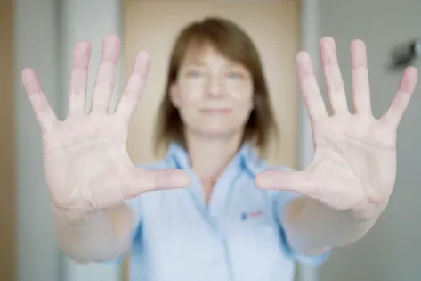 Vrouw in uniform met uitgestrekte handen naar voren gericht, focus op de handen.