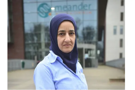 Ziekenhuisschoonmaakster met hoofddoek staat buiten voor de ingang van het Meander Medisch Centrum, symbool voor haar werk in de eerste linie van de coronabestrijding.