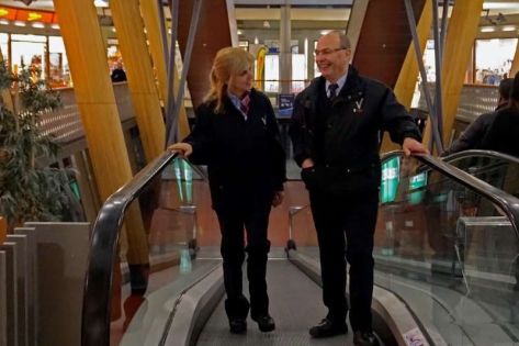 Directeur Trigion in vermomming en uniform loopt mee met een mannelijke beveiliger in uniform in het winkelcentrum op een roltrap.