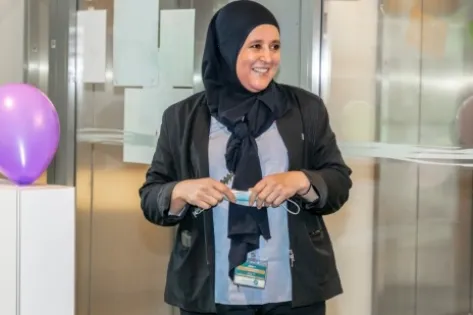 Blije medewerker van Gom komt uit de lift en wordt verrast door een feestelijke ontvangst, met ballonnen en collega’s in de achtergrond.