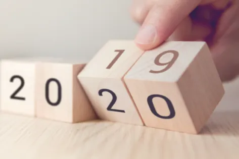 Hand draait een houten blokje van 2019 naar 2020 om, symbool voor de overgang naar het nieuwe jaar.